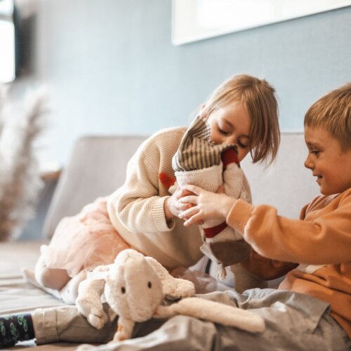 Chłopiec i dziewczynka bawiące się pluszowymi zabawkami na kanapie.
