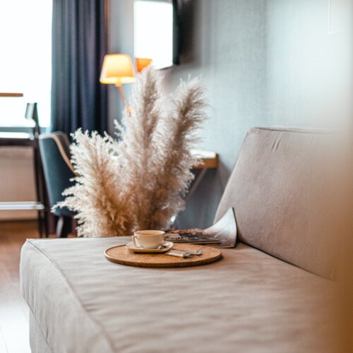 Filiżanka kawy na okrągłej tacce, leżące na kanapie w apartamencie hotelowym.