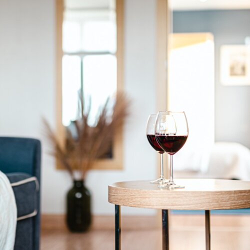 Dwa kieliszki wina stojące na okrągłym, drewnianym stoliku kawowym.