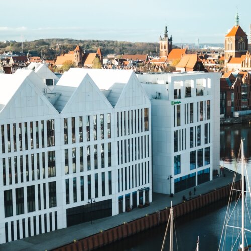 Biały spichlerz znajdujący się na nabrzeżu rzeki ze Starym Miastem w Gdańsku w tle.