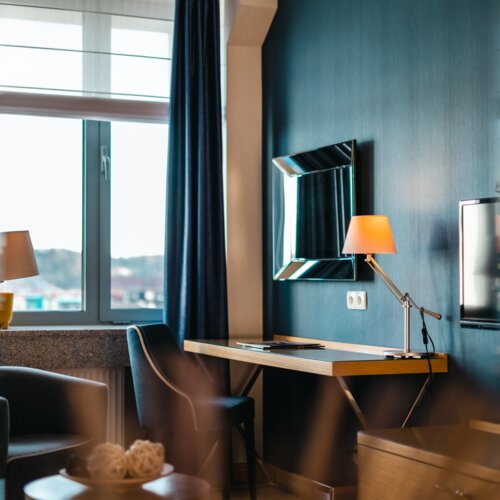 Biurko z fotelem, lampą i lustrem zawieszonym na granatowej ścianie.