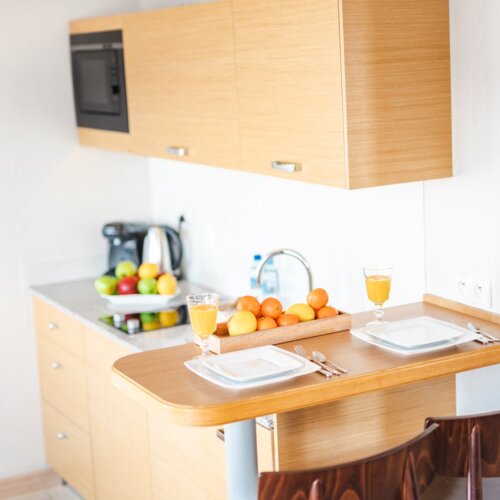 Stolik barowy z biała zastawą dla dwóch osób i owocami przy aneksie kuchennym.