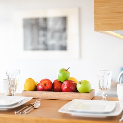 Stolik barowy z biała zastawą dla dwóch osób i owocami z obrazem w tle.