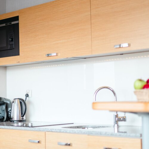 Aneks kuchenny z drewnianymi frontami, zlewem i czajnikiem w apartamencie hotelowym.