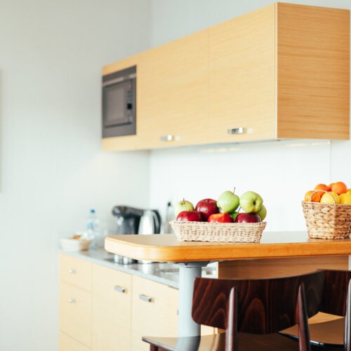 Czerwone i zielone jabłka w wiklinowym koszyku stojące na blacie aneksu kuchennego.