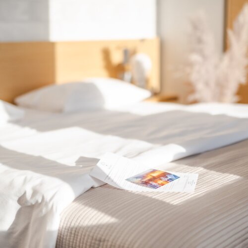 List powitalny i pocztówka leżąca na łóżku hotelowym.