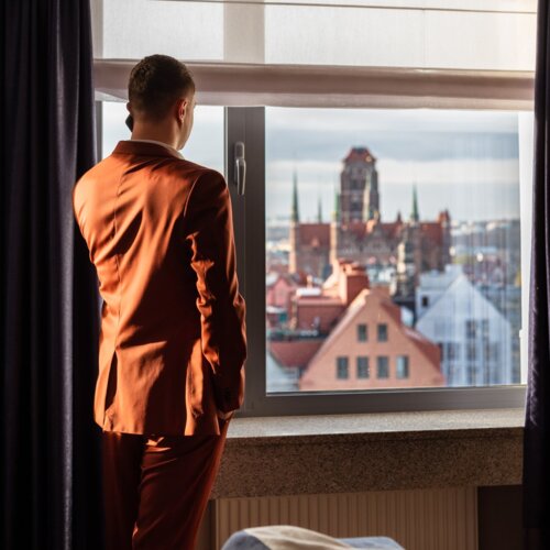 Mężczyzna w czerwonym garniturze podziwiający przez okno widok na gdańskie Stare Miasto.