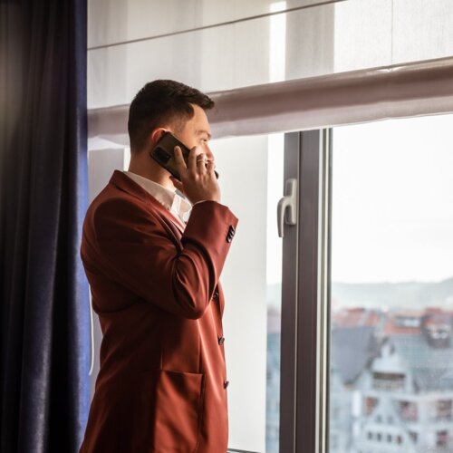 Mężczyzna w czerwonym garniturze, rozmawiający przez smartfon i patrzący przez okno.