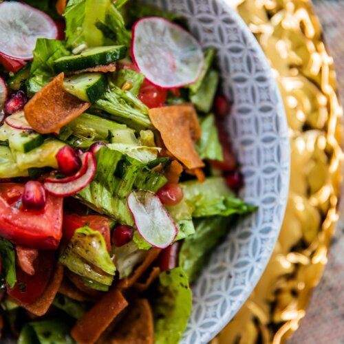 Ein Teller mit einem Salat bestehend aus grünem Gemüse, Tomaten, Radieschen, Granatapfel nd Olivenöl