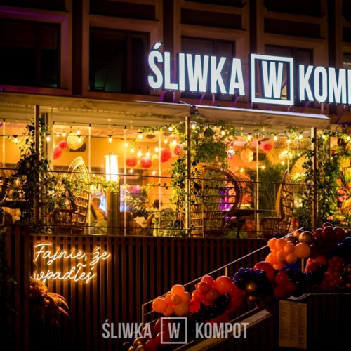 Restauracja z przytulnym oświetleniem, roślinną dekoracją i wygodnymi wiklinowymi fotelami na zadaszonym tarasie.