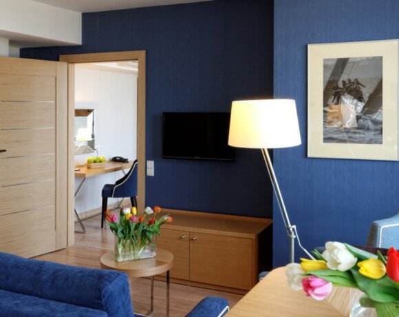 Telewizor, lampa i kwiaty w pokoju dziennym apartamentu hotelowego.