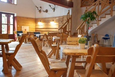 Wnętrze izby pełne drewnianych stołów oraz krzeseł.