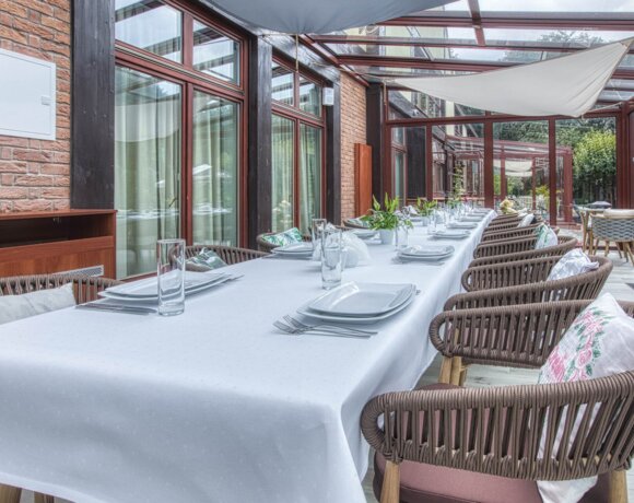 Nakryty w biały obrus oraz zastawę stołową długi stół w oranżerii.