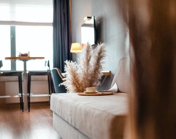 Modern hotel room with a comfortable sofa, tray holding a coffee cup, pampas grass décor, and a table by the window