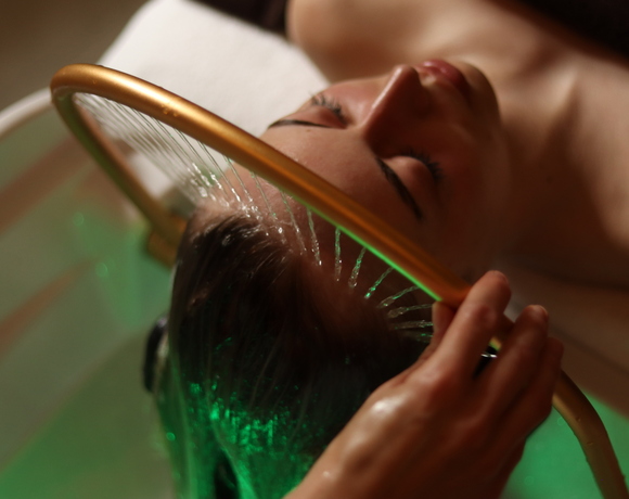 Gość relaksuje się podczas aromatycznego masażu głowy z wodą w luksusowym spa hotelowym.