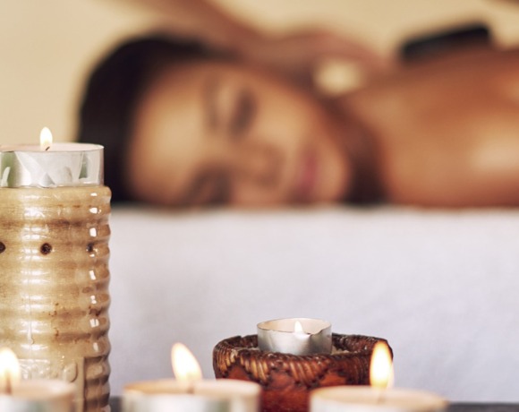 Žena relaxuje při masáži ve wellness s hořícími svíčkami vytvářejícími klidnou atmosféru.