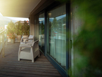 Private hotel balcony with wicker chairs, potted plants, sliding glass doors, glass railing, wooden deck and mountain view