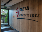 Holzverkleidete Lobby mit META apartments-Schriftzug an der Wand, Glastür zum grünen Außenbereich und Fußmatten am Eingang.