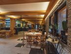Gemütliches Hotelrestaurant mit sichtbaren Holzbalken, steinerner Akzentwand, runden Holztischen, Bar- und Buffetbereich, Pflanzen auf der Fensterbank