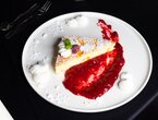 Stück Käsekuchen mit Puderzucker, Sahne, Himbeere und Minze, serviert mit Himbeercoulis und Baiser-Tupfen auf weißem Teller