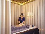 Spa-Therapeutin in dunkelblauer Uniform bei entspannender Massage auf weicher Behandlungsliege, sanfte Vorhänge und warmes Licht
