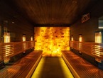 Infrarot-Sauna mit hinterleuchteter Himalaya-Salzwand, Holzbänken beidseits und warmem bernsteinfarbenem Licht zur Entspannung.