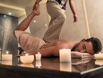 Mann erhält Fußmassage auf Spa-Liege, umgeben von Kerzen, Marmorwänden und einem Handtuch unter dem Kopf.