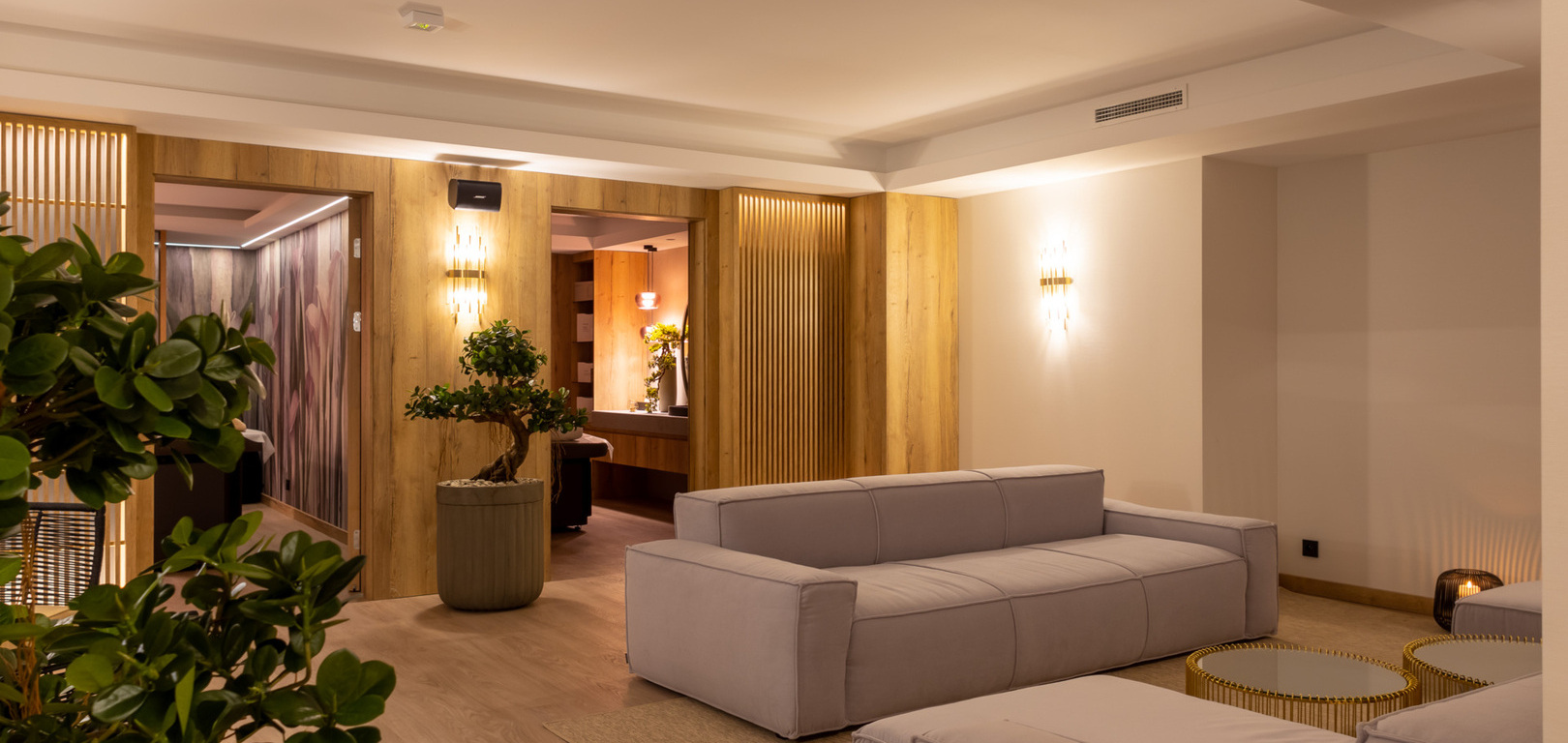 Moderne Hotel-Lounge mit grauen Polstersofas, warmen Holzakzenten, stimmungsvoller Beleuchtung und Zimmerpflanzen