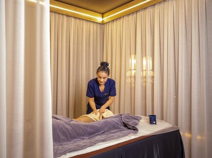 Spa-Therapeutin in dunkelblauer Uniform bei entspannender Massage auf weicher Behandlungsliege, sanfte Vorhänge und warmes Licht