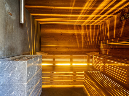 Holzsauna im Hotel mit mehrstufigen Bänken, Saunaofen mit Steinen und warmem bernsteinfarbenem Licht.