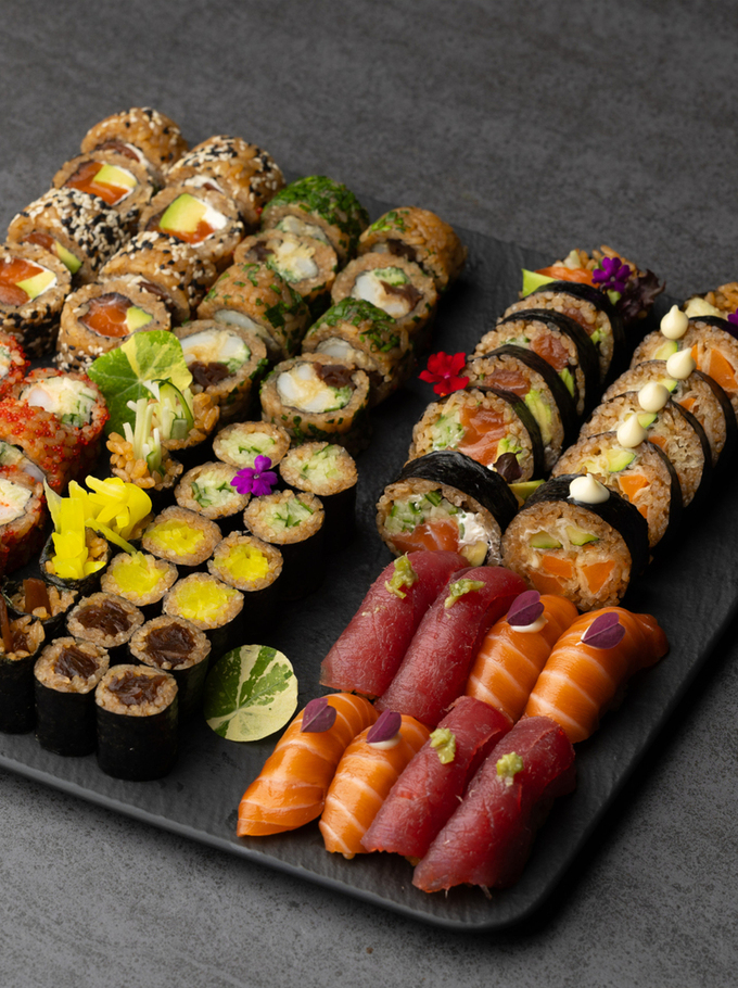 Vielseitige Sushi-Platte auf Schiefer — Lachs- und Thunfisch-Nigiri, verschiedene Maki mit Avocado, Sesam, Tobiko und essbaren Blüten