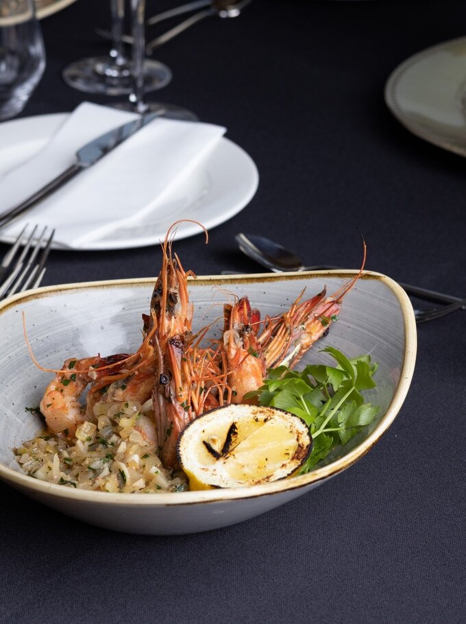 Gegrillte Garnelen mit gegrillter Zitrone, Kräuterreis und Salat in Keramikschale auf elegantem schwarzen Tisch mit gefalteter Serviette