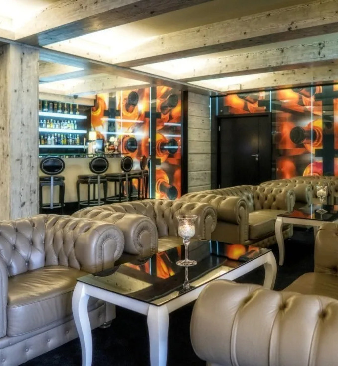 Intimate cocktail lounge with tufted leather Chesterfield sofas, glossy tables, illuminated bar and warm wooden beam ceiling