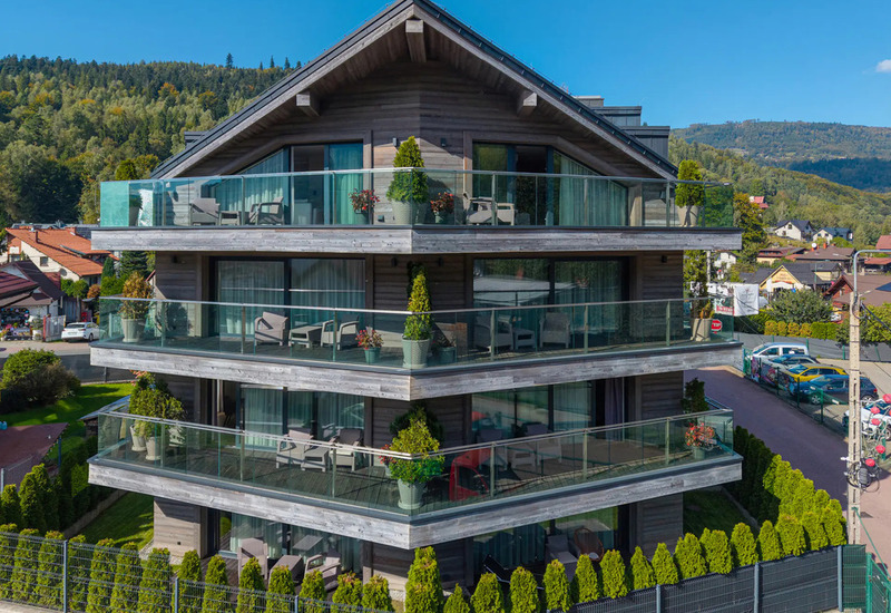 Three-story chalet-style hotel with spacious glass-railed balconies, outdoor seating on terraces and mountain views