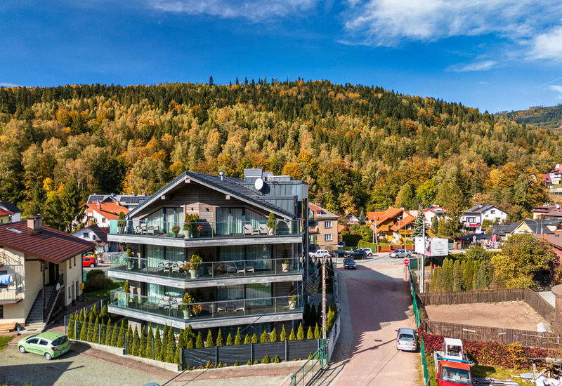 Modern chalet-style guesthouse with glass balconies and furnished terraces overlooking autumn forested hills and village.