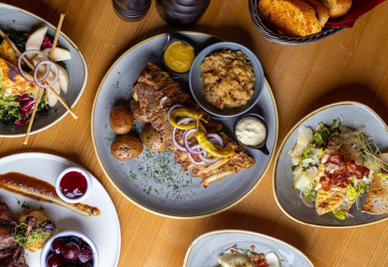 Grilled ribs with roasted baby potatoes, pickled peppers, mustard and sauerkraut, with salads and bread on a wooden table