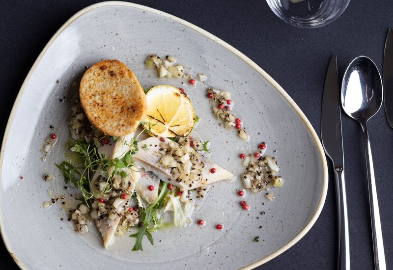 Fine-dining starter: smoked fish fillets with diced onion relish, microgreens, grilled lemon and crostini