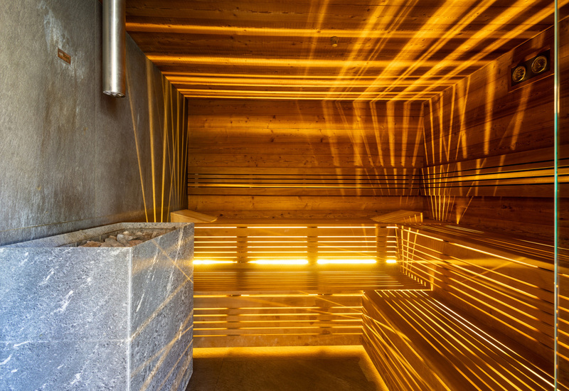 Wood-lined hotel sauna with tiered benches, stone heater with sauna rocks and warm amber lighting.