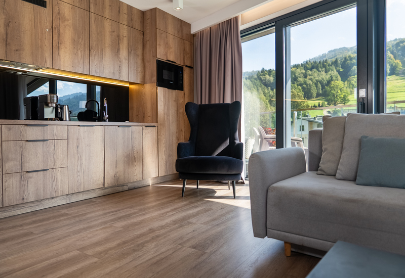 Studio living area with wood kitchenette, espresso machine and microwave, comfy armchair, balcony with mountain view