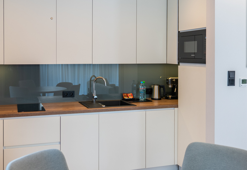 Modern kitchenette with white cabinets, wood countertop, chrome sink, induction hob, microwave and coffee machine.