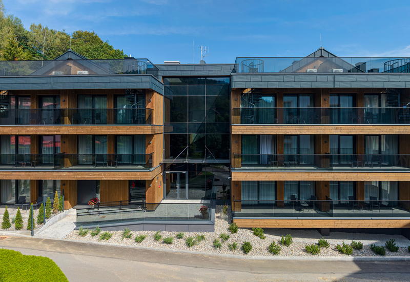 Modern wooden hotel with glass balconies, floor-to-ceiling windows, rooftop terraces and spiral stairs overlooking forested mountain views