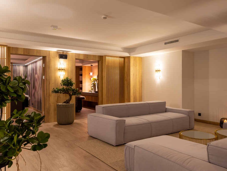 Ruhige Hotellounge mit grauen Polstersofas, warmen Holzpaneelen, Bonsai im Topf, sanfter Wandbeleuchtung und Spa-Bereich