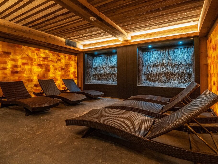 Entspannungsraum im Spa mit beleuchteter Himalaya-Salzwand, geflochtenen Liegen, Schilfnischen mit blauer Beleuchtung und warmen Holzdeckenbalken.