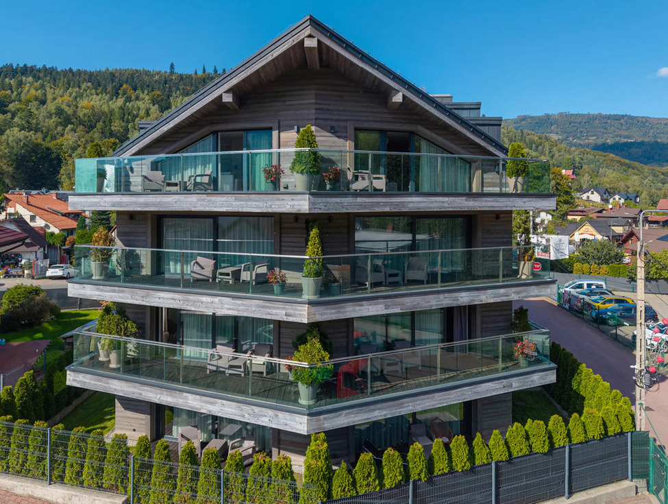 Dreistöckiges Chalet-Hotel mit großzügigen Glasbalkonen, Sitzbereichen auf den Terrassen und Bergblick