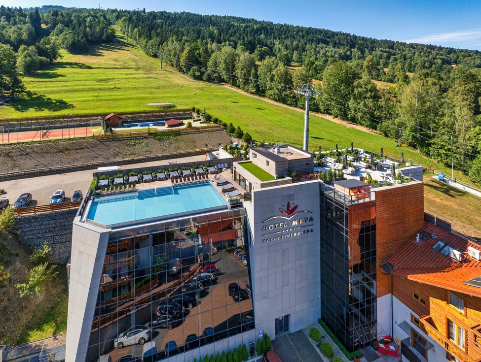 Modern mountain hotel with rooftop pool and sunbeds, terrace lounge, visible ski lift and green hillside views