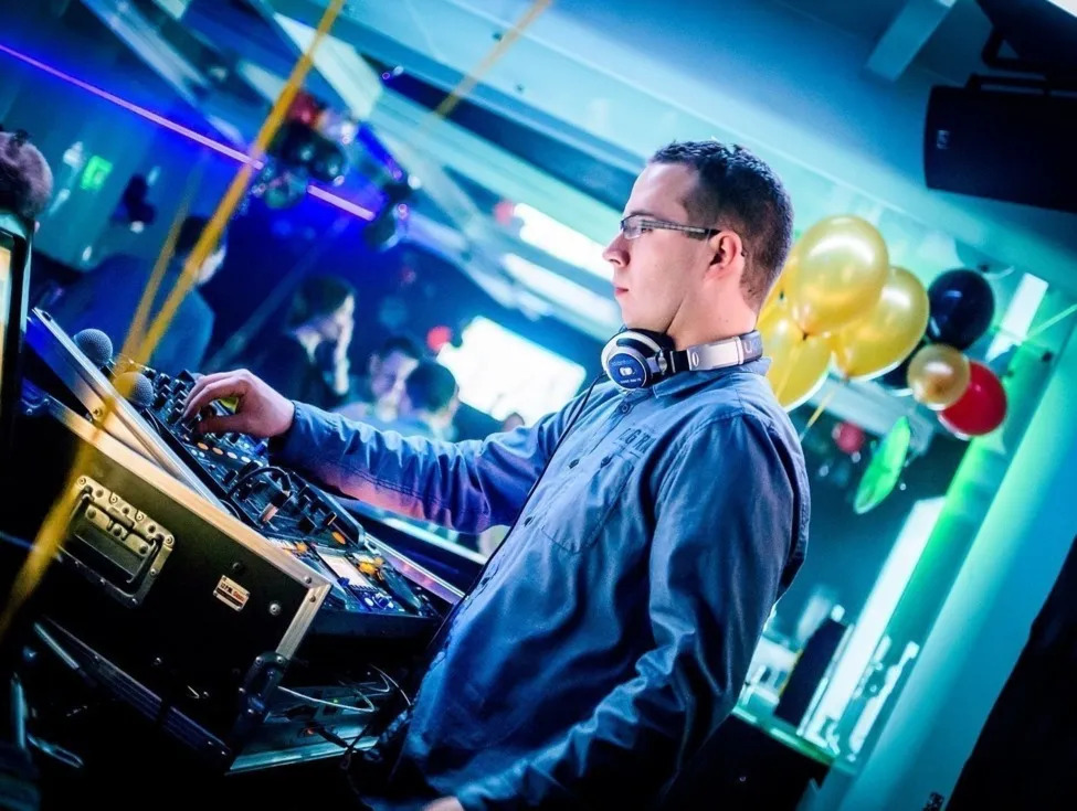Live DJ mixing at a hotel lounge with headphones, illuminated console, balloons and colorful party lighting