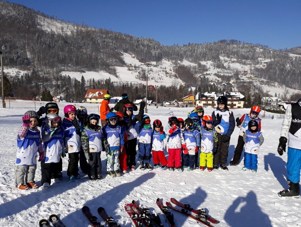 Children in colorful helmets and ski vests with instructors on a family ski slope, snow-covered hills and chalet lodges
