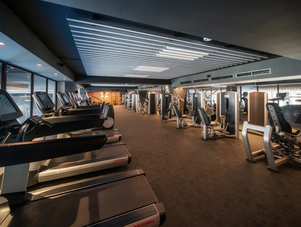 Geräumiges Hotel-Fitnessstudio mit Laufbändern an bodentiefen Fenstern, modernen Kraftgeräten und gedämpfter Beleuchtung