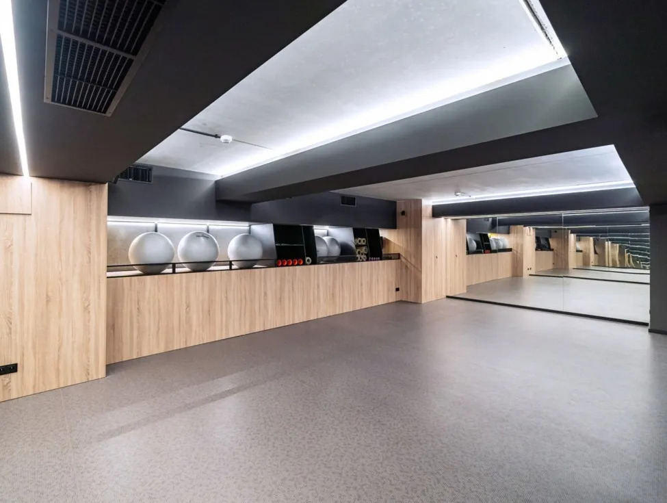Helles, modernes Hotel-Fitnessstudio mit Gymnastikbällen, großem Spiegel, Holzverkleidung und sanfter Deckenausleuchtung für Kurse