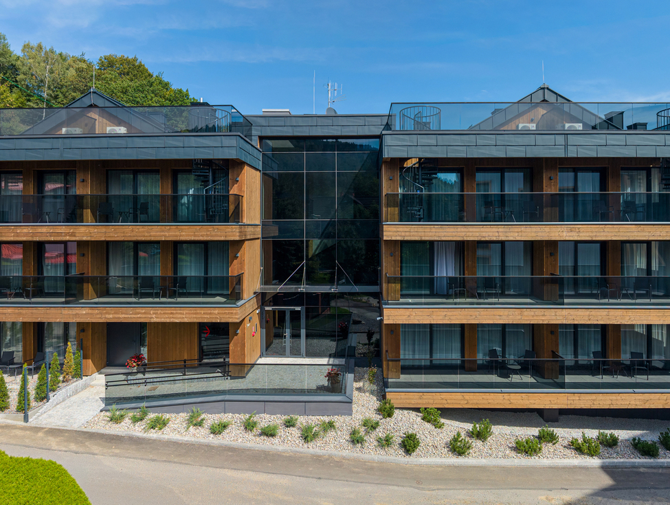 Modernes Holzhotel mit Glasbalkonen, bodentiefen Fenstern, Dachterrassen und Wendeltreppen mit Blick auf bewaldete Berge
